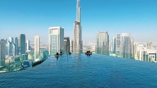 Une piscine à débordement avec des chaises longues, une vue sur les gratte-ciel de la ville et le Burj Khalifa en arrière-plan.