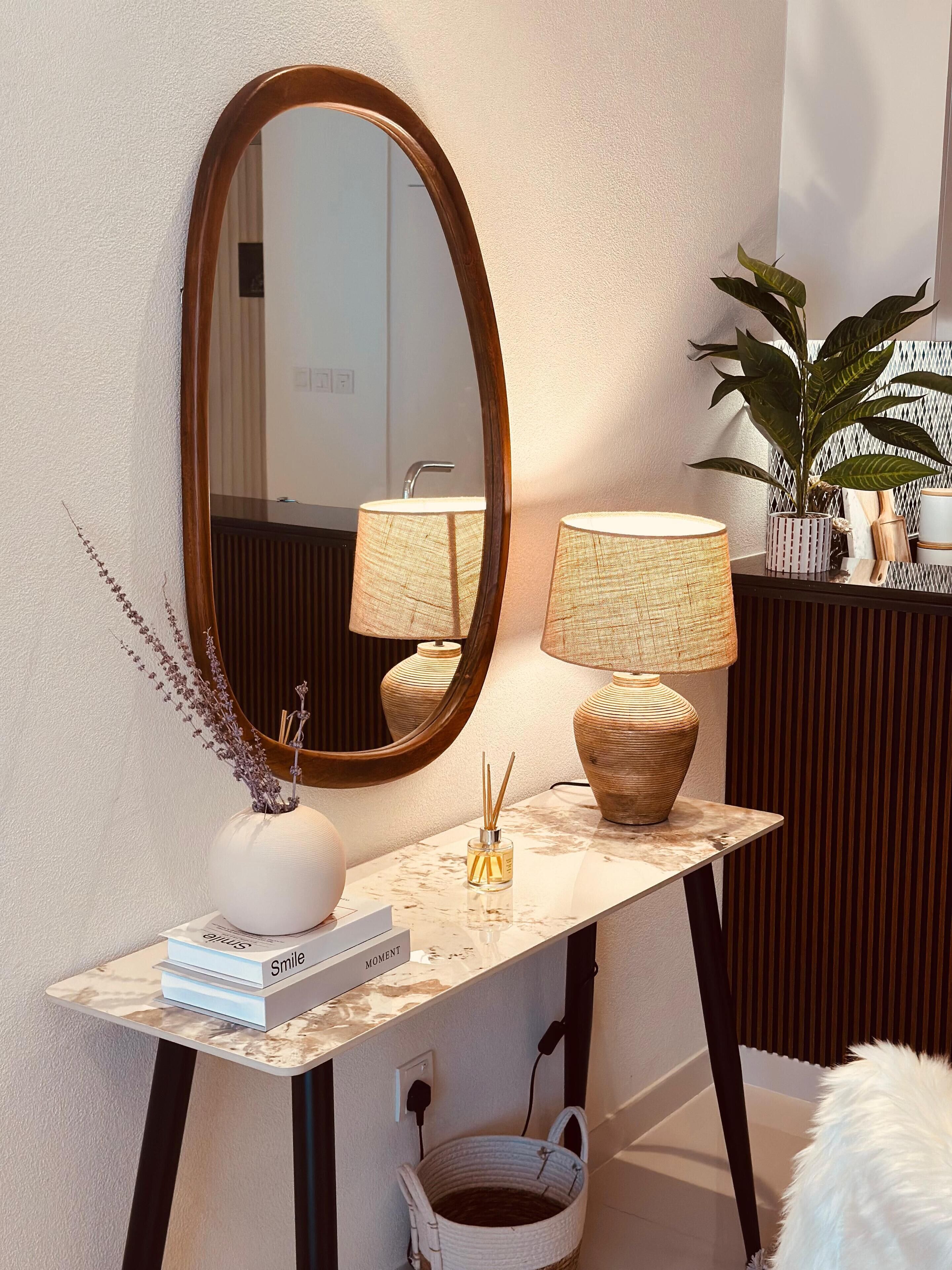 Een wastafel met spiegel, een lamp, een vaas met gedroogde bloemen en een klein mandje.