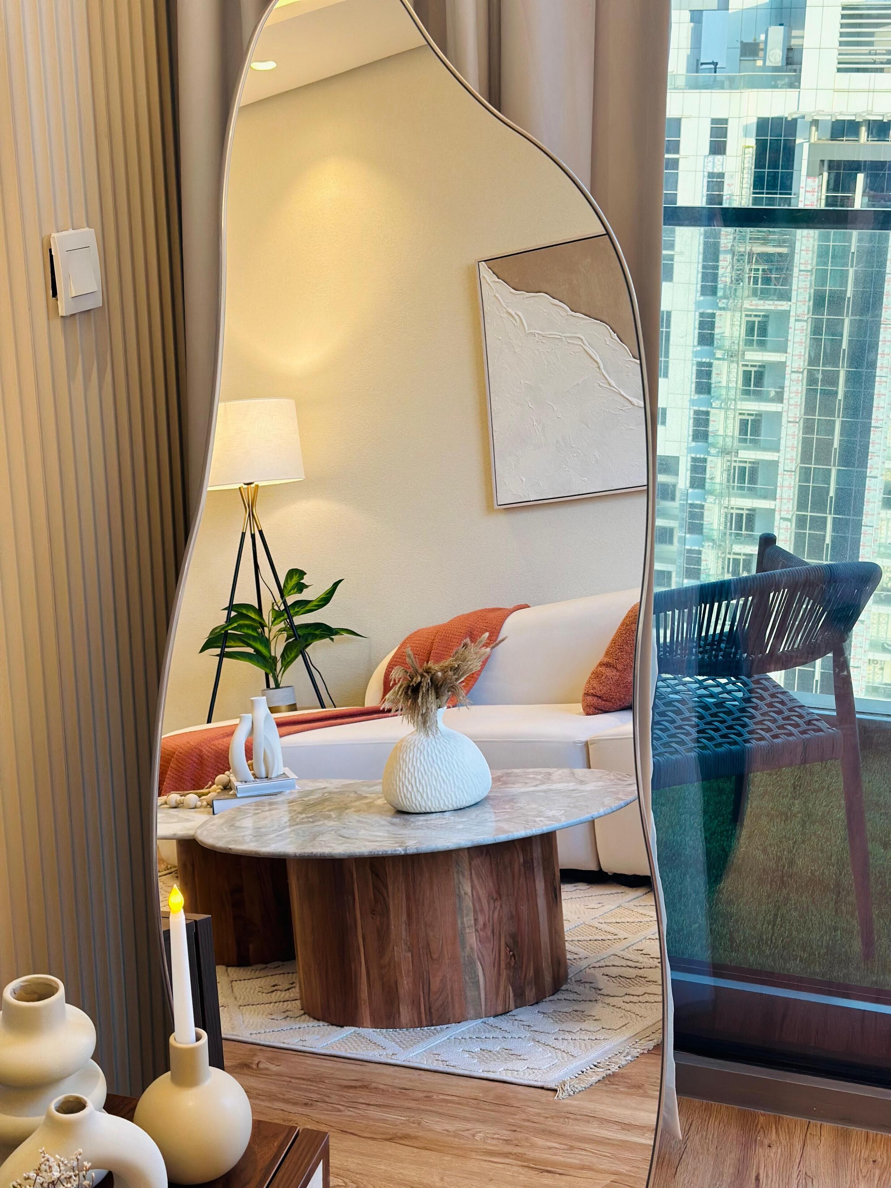 A modern living room with a round coffee table, a sofa, a mirror, and a view of a cityscape through a window.