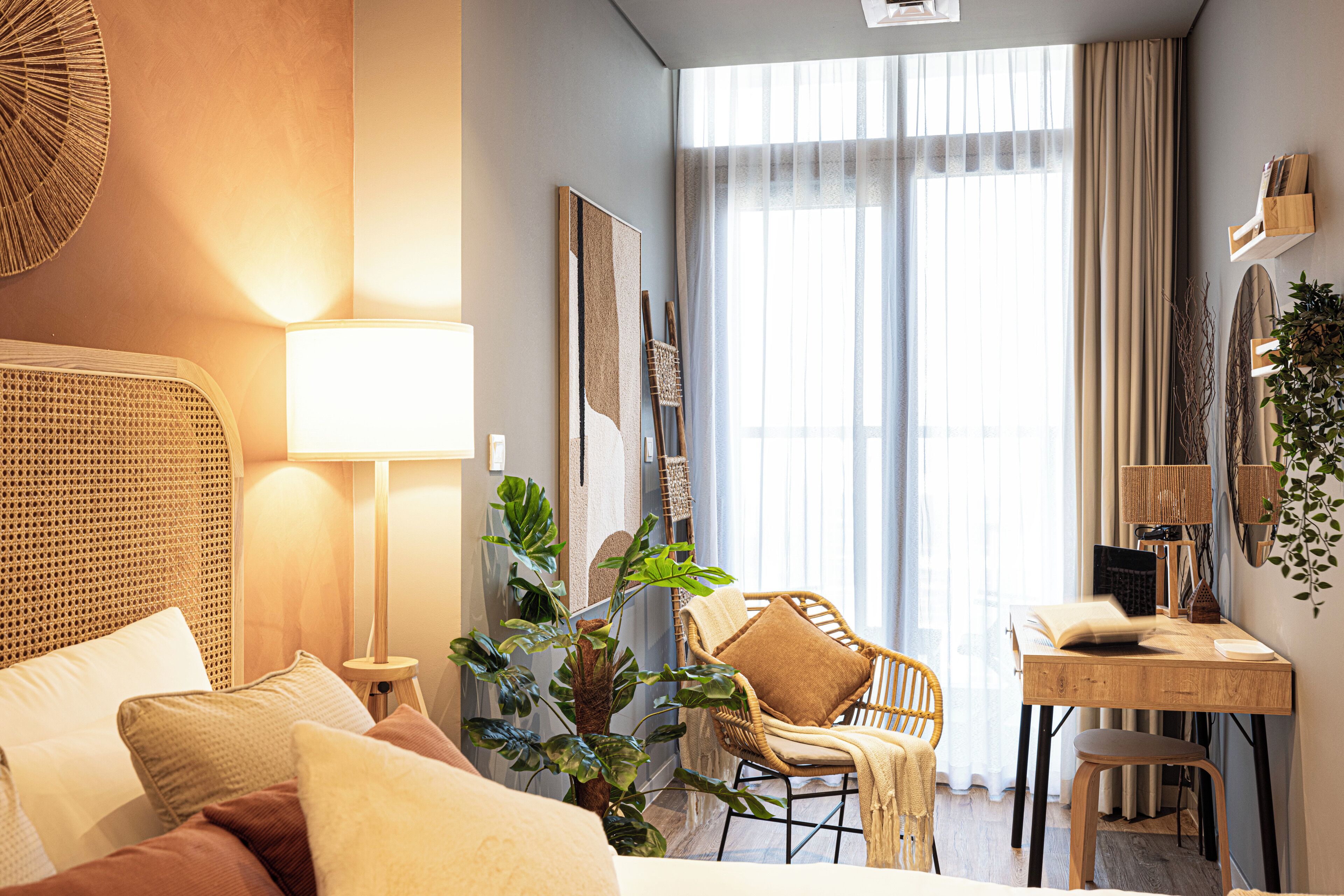Een moderne hotelkamer met een bed, een bureau, een stoel en een groot raam met gordijnen.