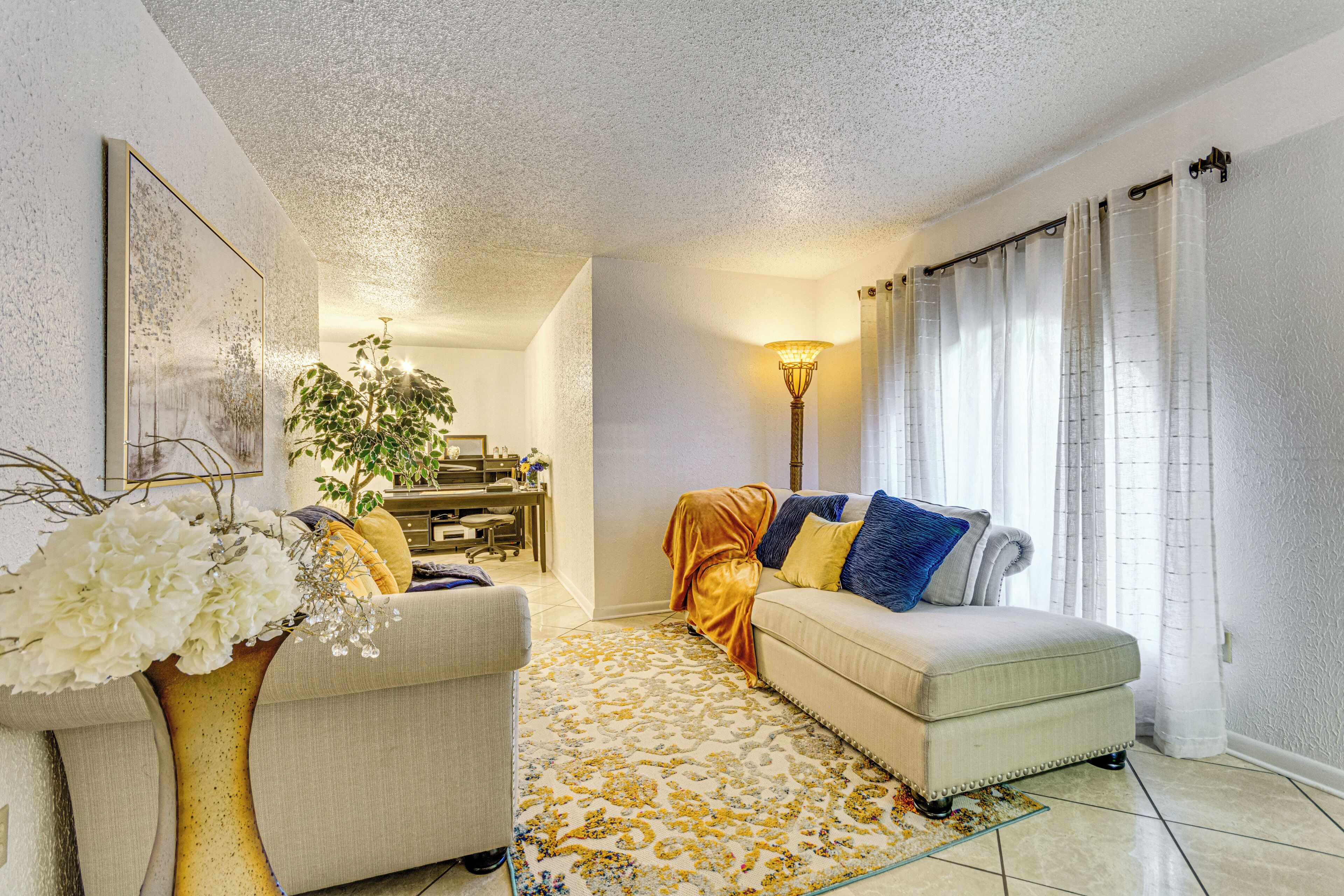 A living room with a sofa, a coffee table, a lamp, and a decorative vase with flowers.
