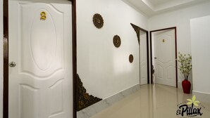 Un couloir avec des portes blanches numérotées 2 et 4, des rosaces décoratives sur les murs et un vase rouge contenant des fleurs blanches.