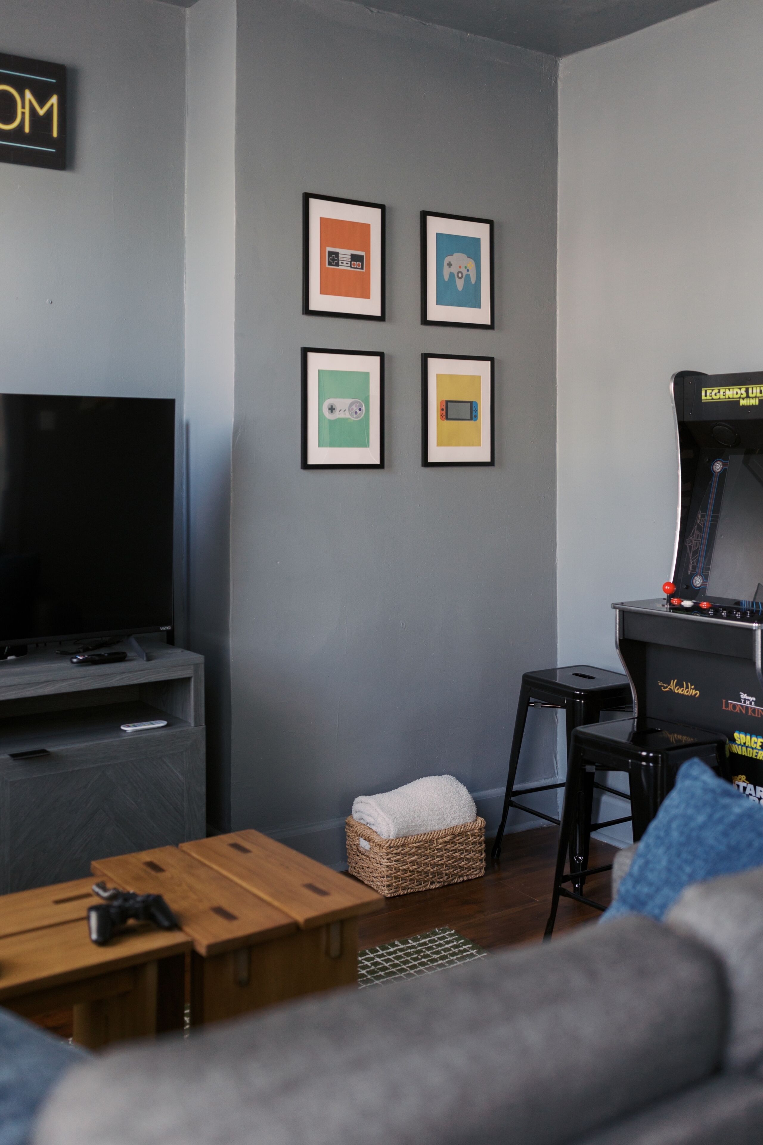 Ein Wohnzimmer mit Flachbildfernseher, Spielkonsole, Couchtisch, Sofa und einem kleinen Tisch mit Korb.