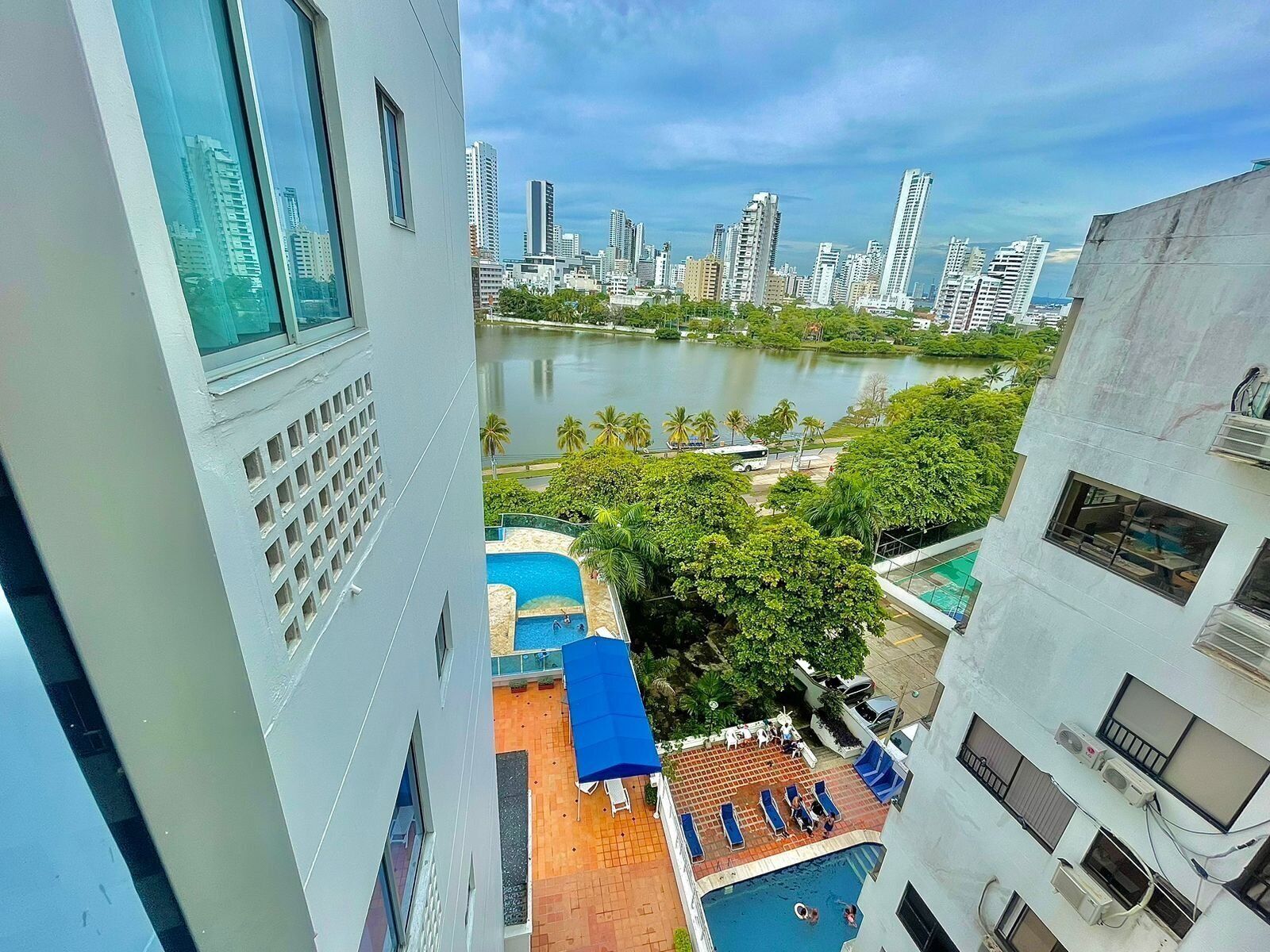 A high-rise building with a view of a city skyline, a body of water, and a pool area with lounge chairs and umbrellas.