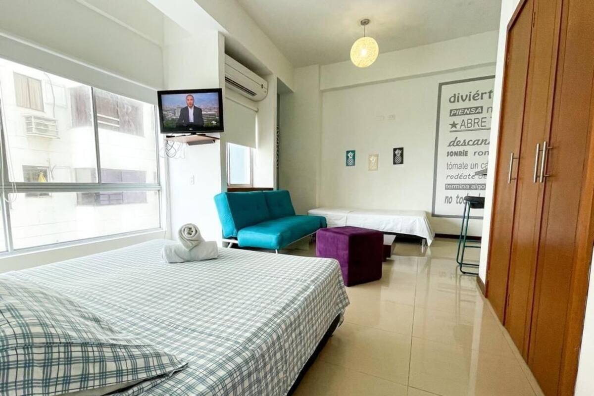 Habitación de hotel con cama, sofá, televisor y un ventanal grande.