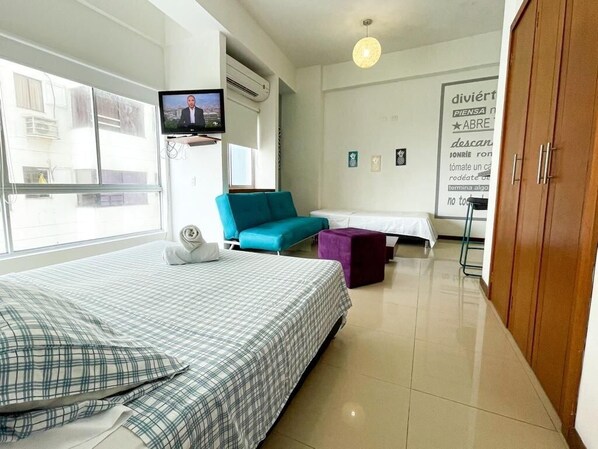 Habitación de hotel con cama, sofá, televisor y un ventanal grande.