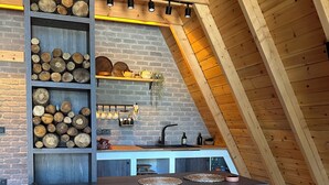 A modern kitchen with a brick wall, wooden beams, and a sloped ceiling. It features a built-in shelf with logs, a sink, and stools. - Chalet Sapanca (Sapanca)