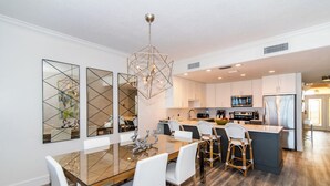 A modern kitchen with white cabinets, a central island, and a dining area with a glass table and white chairs.