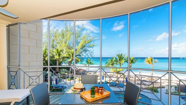 A dining area with a table and chairs, a view of the beach and ocean, and a large window.
