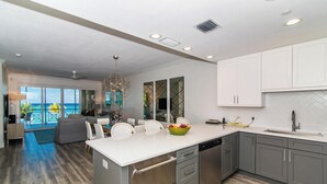 A modern kitchen with a large island, grey cabinets, and a view of the ocean.