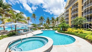 A hotel pool area with a hot tub, lounge chairs, and palm trees.