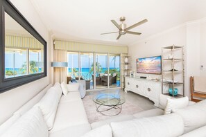 A living room with a sofa, TV, and a view of the ocean.
