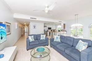A spacious living area with a ceiling fan, a kitchen in the background, and a dining area with a view.