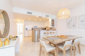 A modern kitchen with white cabinets, a stainless steel island, and a dining area with a glass table and white chairs. - The Meridian Villa 24, Fourth floor, 3BR/3B, Oceanfront, fully equipped. (Seven Mile Beach)