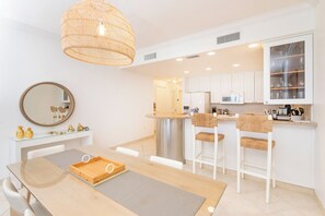Uma cozinha moderna com armários brancos, uma ilha central e uma área de refeições com mesa e cadeiras de madeira.