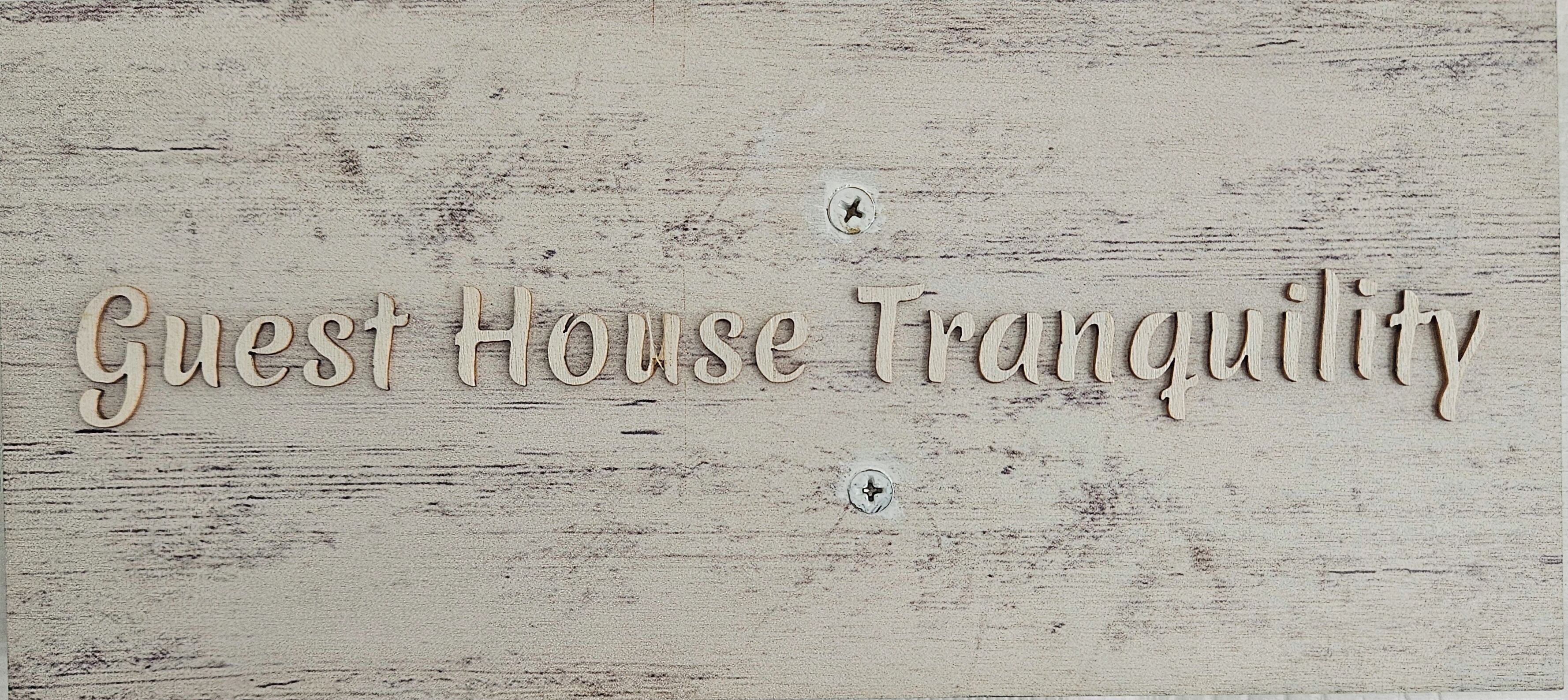A wooden sign with the text 'Guest House Tranquility' in a rustic font.
