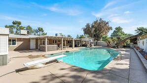 A residential pool area with a clear blue pool, a covered seating area, and a pergola. - Spacious 4BR+Den w/ Pool, Jacuzzi, BBQ, Near Strip (Las Vegas)
