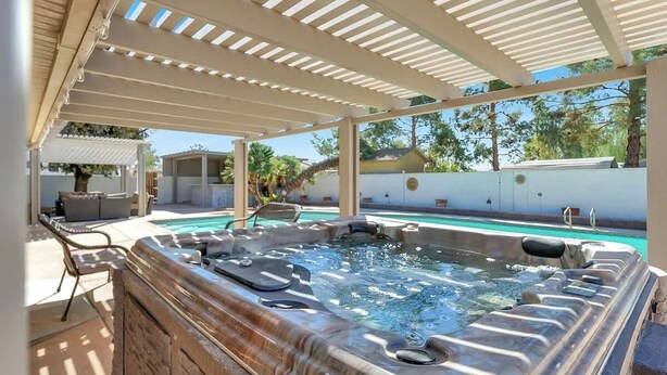 A hot tub under a pergola with a pool in the background. - Spacious 4BR+Den w/ Pool, Jacuzzi, BBQ, Near Strip (Las Vegas)