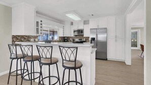 A modern kitchen with white cabinets, stainless steel appliances, and a central island with bar stools. - Spacious 4BR+Den w/ Pool, Jacuzzi, BBQ, Near Strip (Las Vegas)