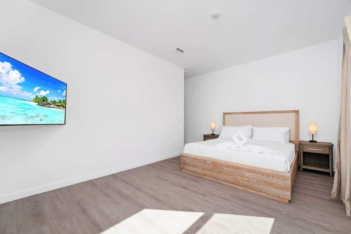 Una habitación de hotel moderna con una cama de madera, un televisor de pantalla plana en la pared y una mesita de noche con lámpara.