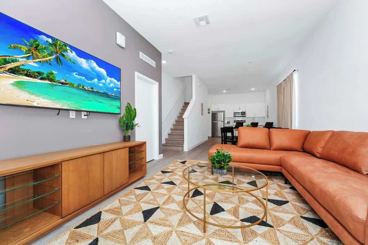 A modern living room with a large flat-screen TV, a leather sofa, a geometric patterned rug, and a wooden entertainment unit.
