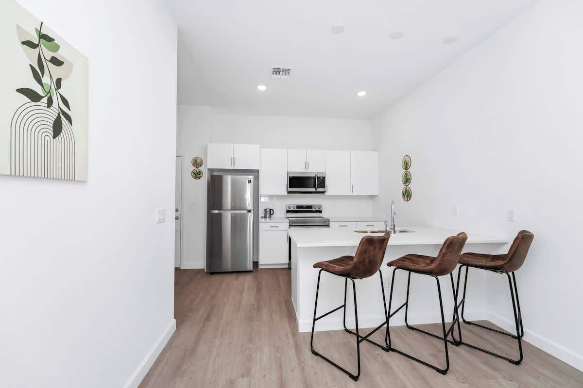 A modern kitchen with white cabinets, stainless steel appliances, and a wooden floor.