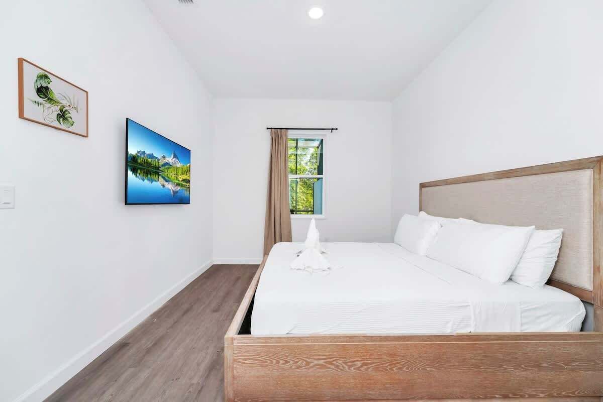 Une chambre à coucher avec un lit en bois, du linge de lit blanc, une fenêtre avec des rideaux et deux tableaux encadrés accrochés au mur.
