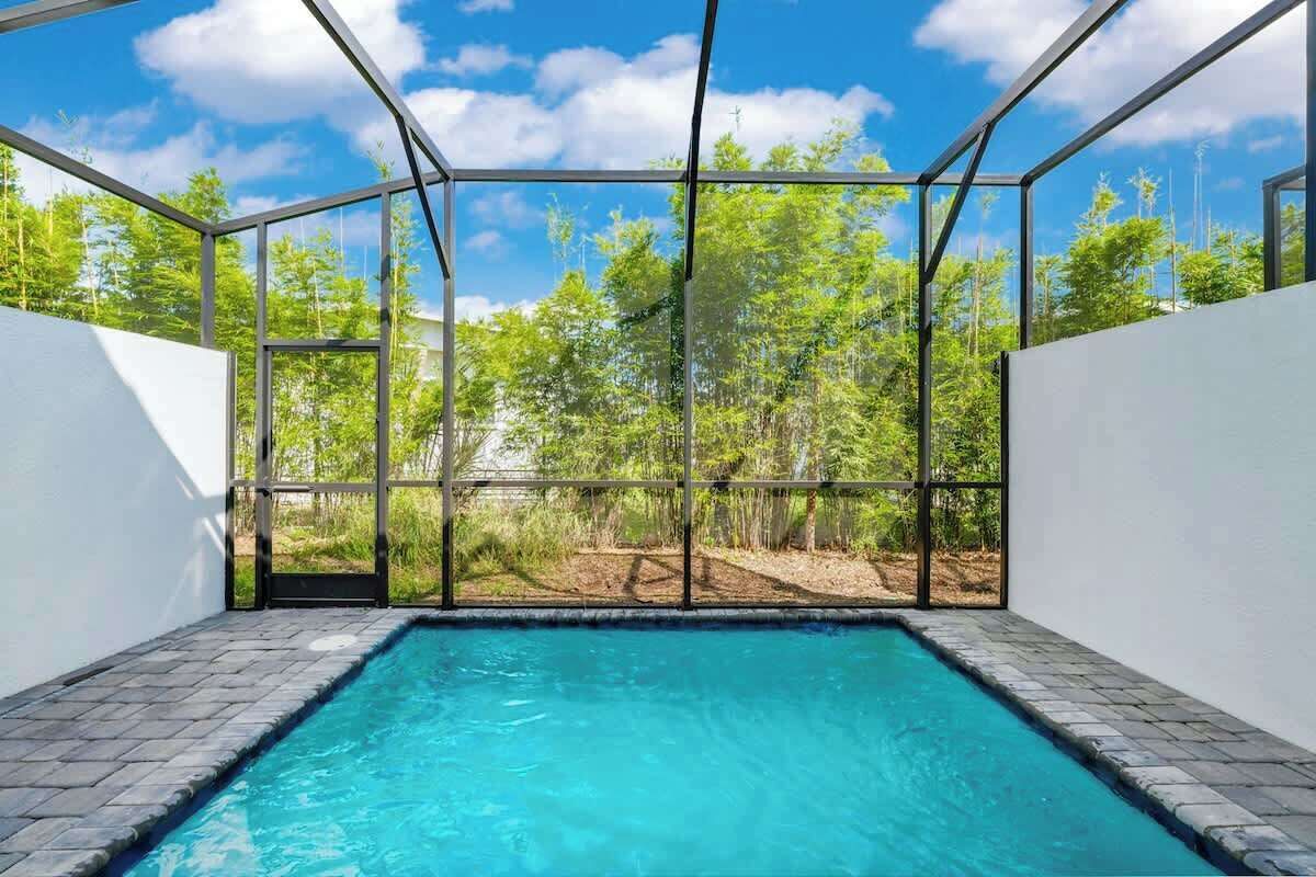 A swimming pool with a glass enclosure, surrounded by a white wall and a view of a forest.