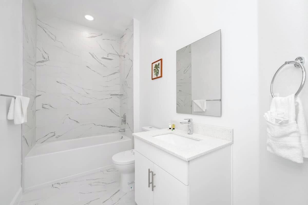 Une salle de bain moderne avec un mur de douche en marbre, un lavabo blanc avec un miroir au-dessus et des toilettes.