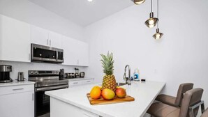 A modern kitchen with white cabinetry, stainless steel appliances, and a central island with fruits.
