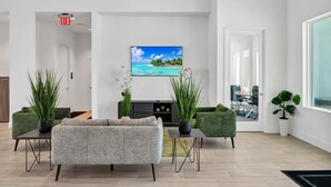 A modern living room with a grey sofa, green armchairs, a flat-screen TV, and potted plants.