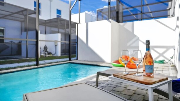 A poolside area with a table, two glasses, and a bottle of wine.