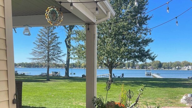A covered porch with a view of a lake, outdoor lighting, and a garden with various plants.