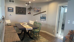 A dining area with a wooden table, chairs, and a rug. There are wall decorations, including a fish and a sign that says "Life is better in water."