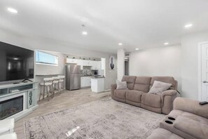 A modern living room with a beige sofa, a fireplace, and a kitchen in the background.