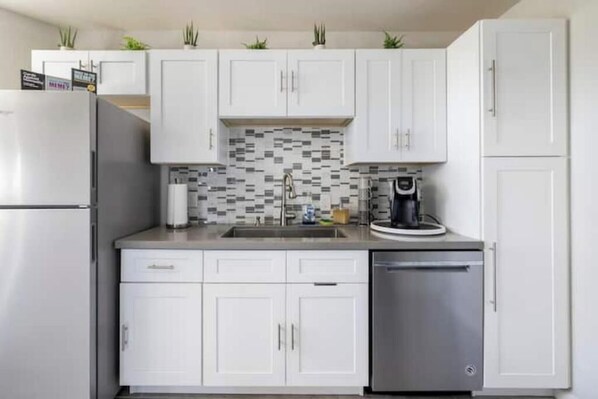 A modern kitchen with white cabinets, a stainless steel refrigerator, a dishwasher, and a tiled backsplash.