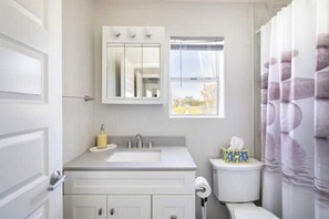 A bathroom with a white sink, mirror, and toilet. There is a window with a view of trees.