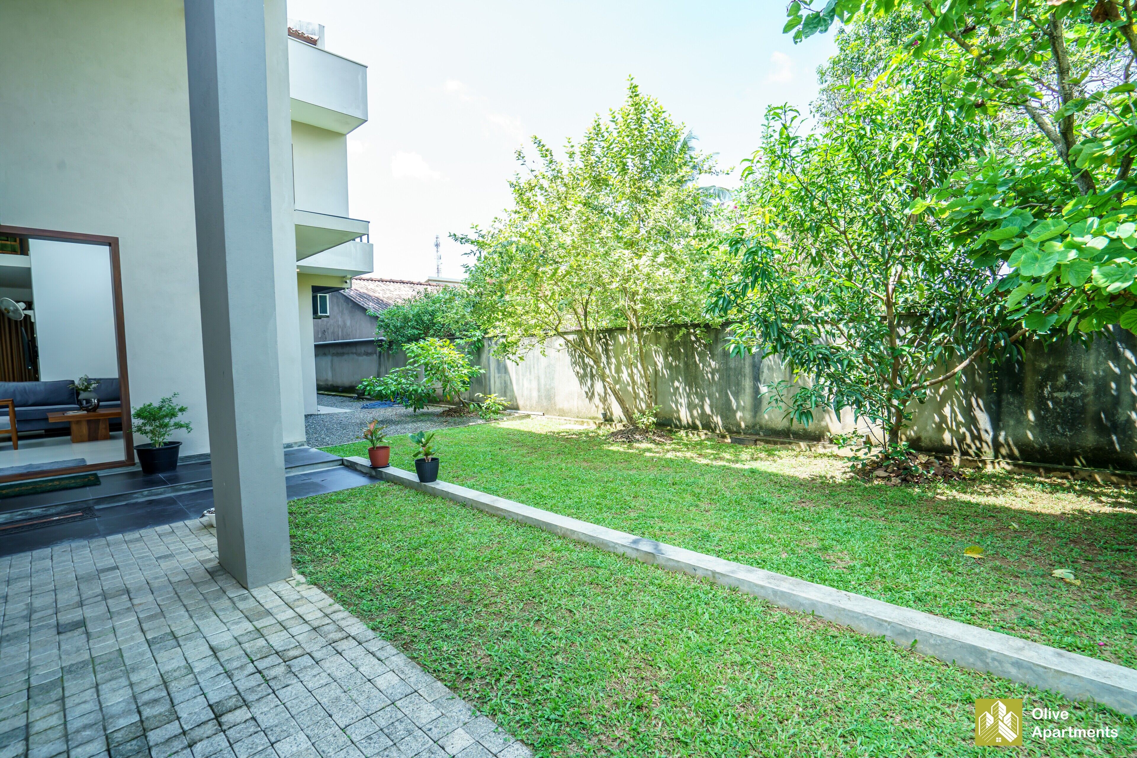 A modern apartment complex with a well-maintained lawn, potted plants, and a concrete pathway leading to a seating area.