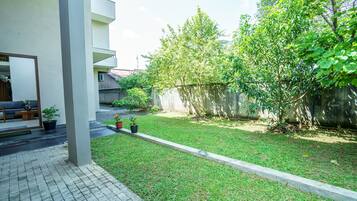 A modern apartment complex with a well-maintained lawn, potted plants, and a concrete pathway leading to a seating area.