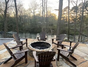 Een terras met een vuurkorf van natuursteen, omringd door houten Adirondack-stoelen.