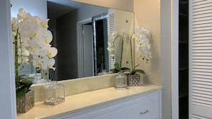 Een badkamermeubel met spiegel, twee orchideeën en een klein glazen vaasje.