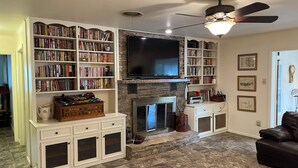 Una sala de estar con chimenea, estanterías, televisor y sofá de cuero.