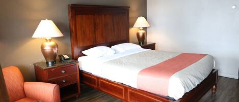 Una habitación de hotel con una cama de madera, dos lámparas de noche, una mesita de noche, una silla y una pequeña mesa.