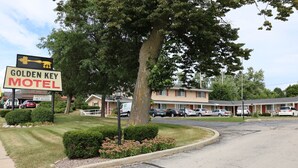 Ein Motel mit einem Schild, auf dem 'Golden Key Motel' und 'Freie Zimmer' steht. Mehrere Autos sind vor dem Haus geparkt, und das Gebäude hat ein rotes Dach und beige Wände.