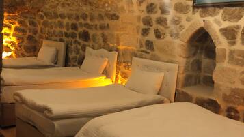 A room with stone walls, two beds, a chandelier, and a painting.