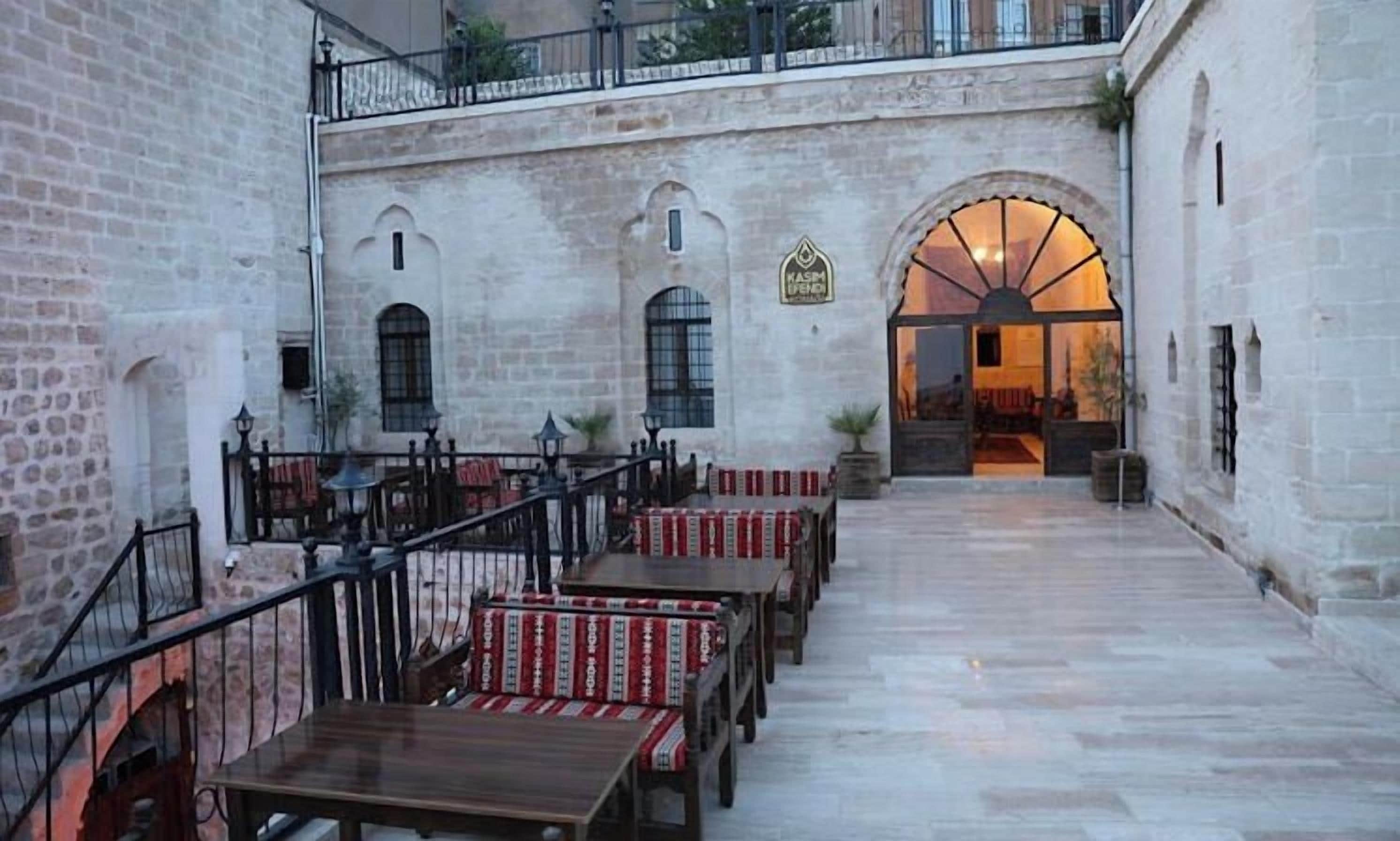 Un patio interior con paredes de piedra, bancos de madera y un arco central.