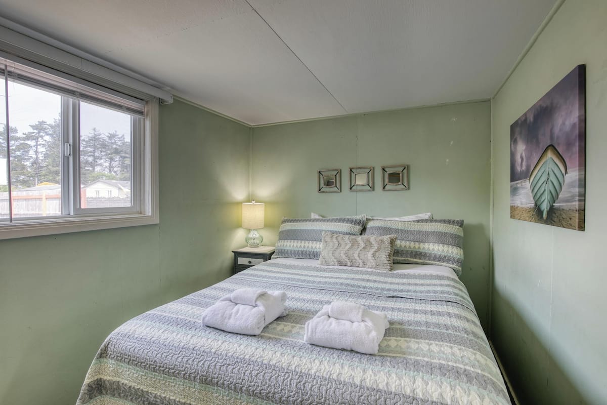 A neatly made bed with striped bedding and two towels, a bedside lamp, and a framed picture on the wall.