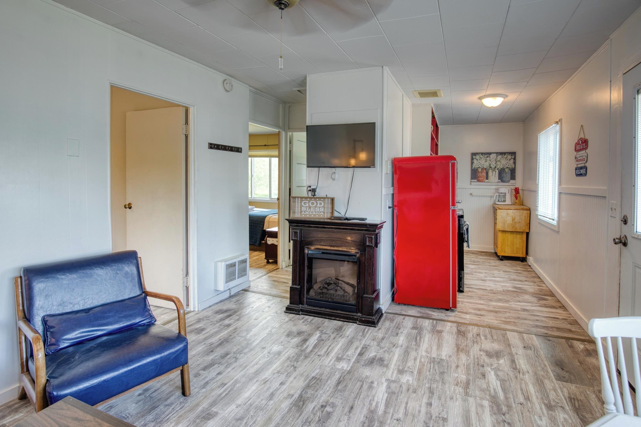 A room with a blue leather chair, a fireplace, a red refrigerator, and a television mounted on the wall.
