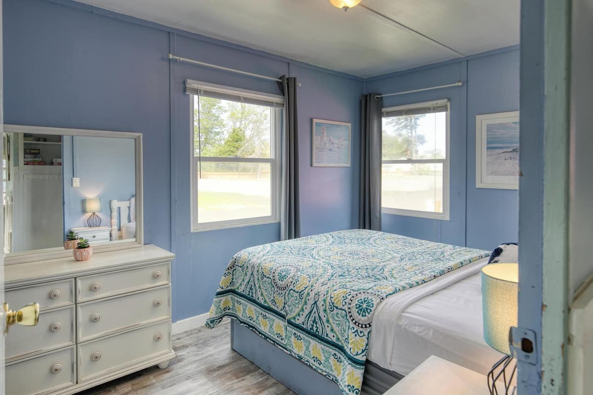 A bedroom with a bed, dresser, and two windows.