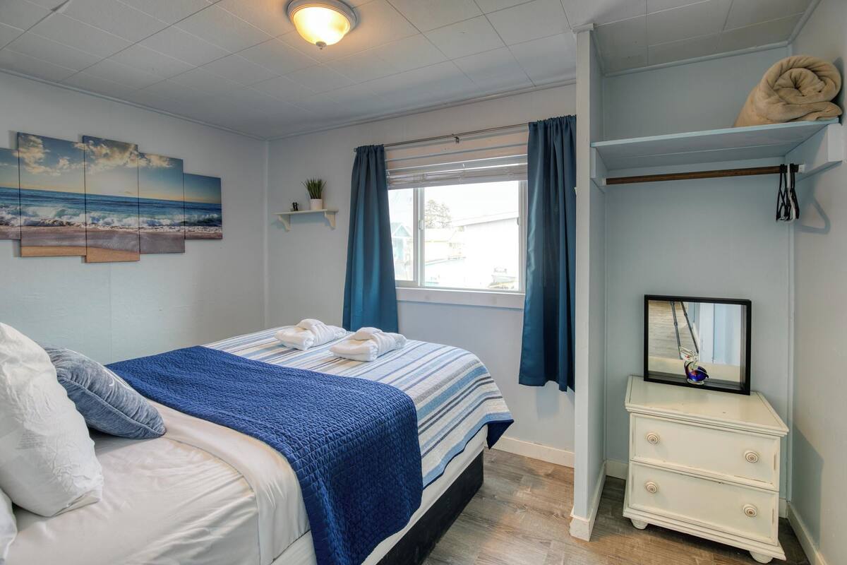 A bedroom with a bed, a dresser, a window with curtains, a painting on the wall, and a ceiling light.